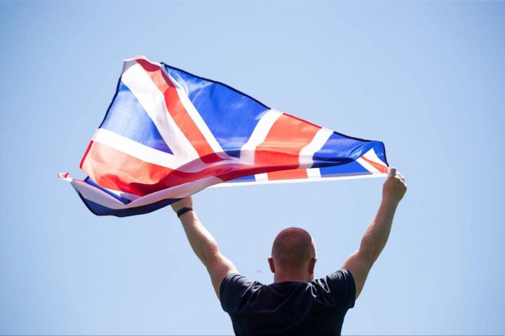 młody mężczyzna stojący na tle nieba z flagą Wielkiej Brytanii